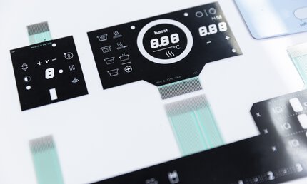 Close-up of a black and white electronic control panel with various buttons and digital displays.