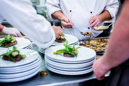 Several chefs stand around a trolley stacked with plates and arrange the food on them in an appealing way.