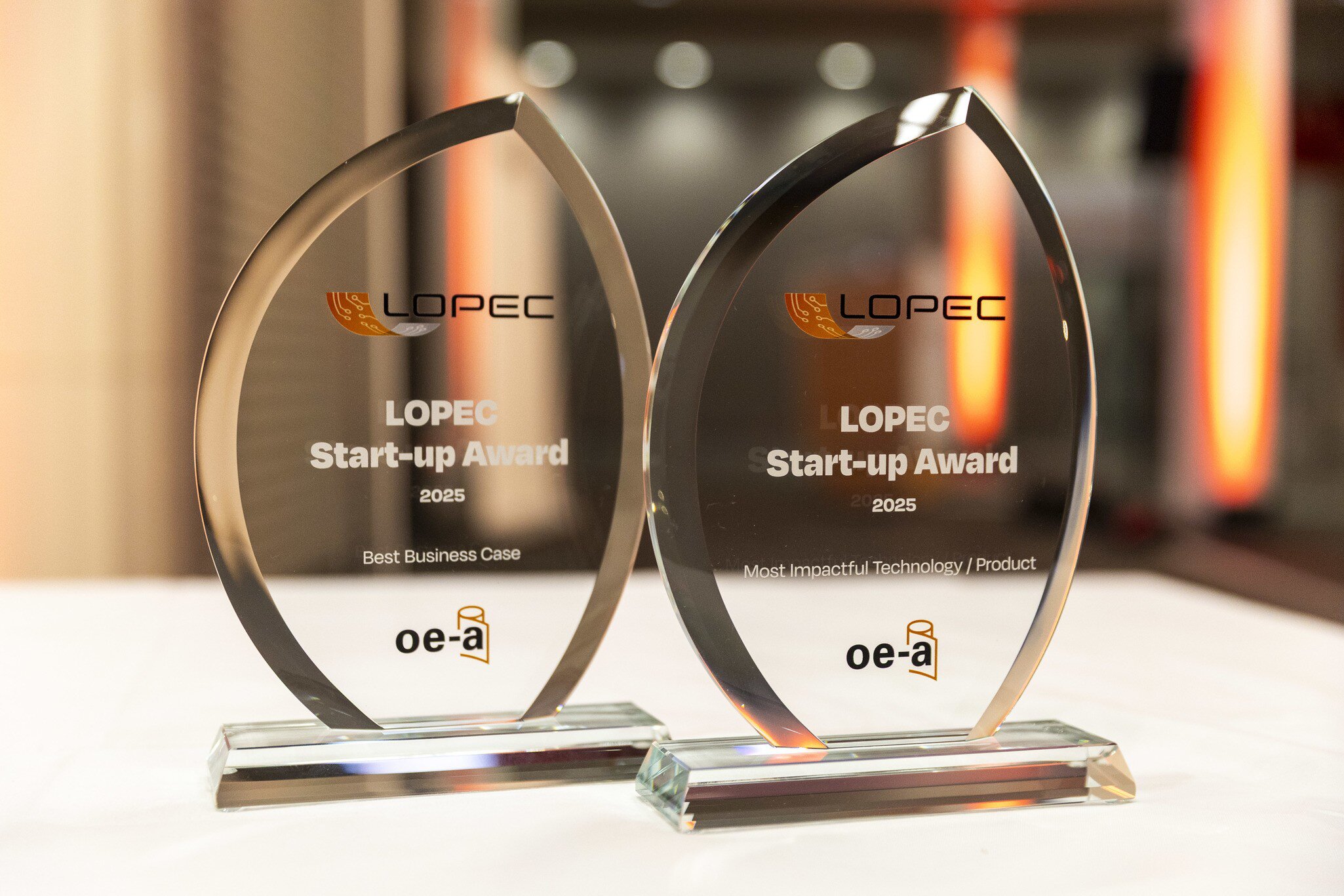 Close-up of two transparent LOPEC Start-up Award 2025 trophies made of glass with a curved metal frame.
