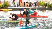 Mann kniet auf einem Stand Up Paddle im Swimminpgool einer Messehalle.