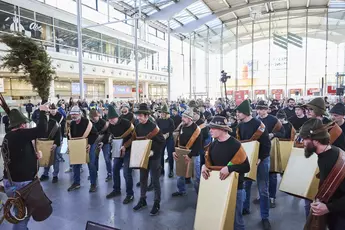 Blick in die menschengefüllte Eingangshalle eines Messegebäudes. Vorne treten Personen mit großen Glocken auf.