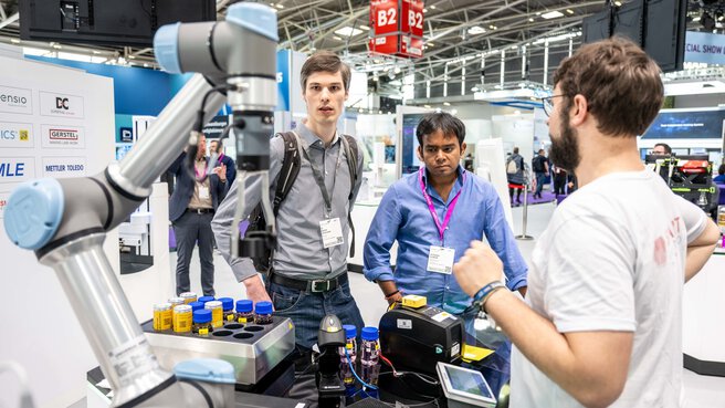 A robot-like laboratory device is presented. Two visitors stand next to it.