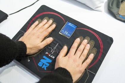 Two hands rest on a heart-shaped sensor mat with a digital display in the center showing a pulse of 74.