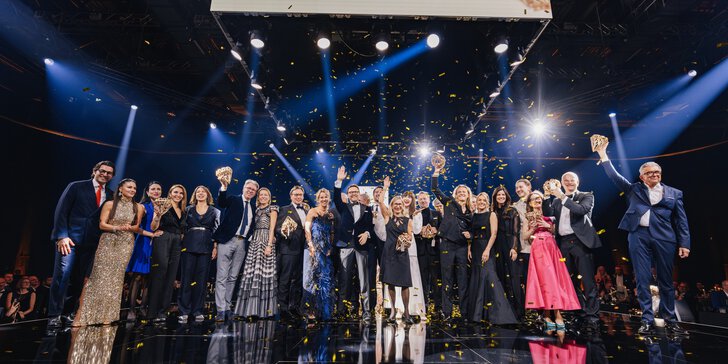 The winners of the INHORGENTA AWARD 2026, dressed in their festive attire, stand on a stage waving to the audience as golden confetti rains down.