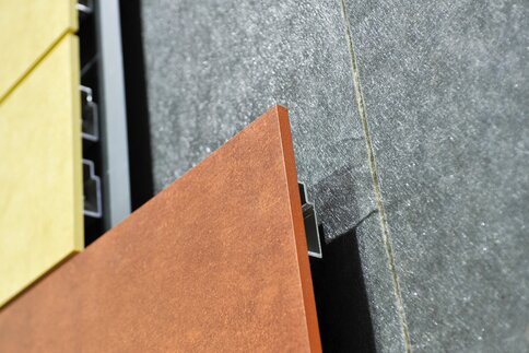 Close-up of the orange, yellow, and gray facade panels with visible fastening clips.