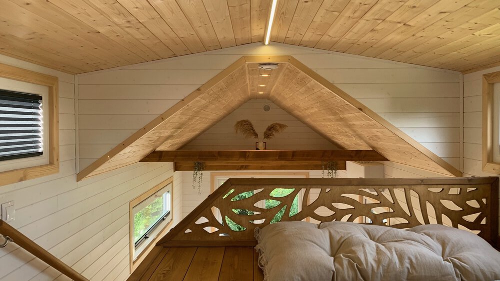Gemütliches Dachgeschossschlafzimmer mit Holzdecke, schrägen Wänden, Bett und kleinem Fenster. Minimalistisches und warmes Design.