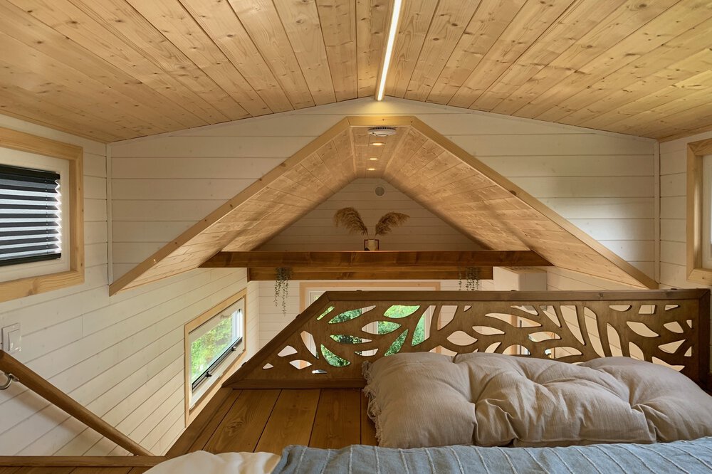 Gemütliches Dachgeschossschlafzimmer mit Holzdecke, schrägen Wänden, Bett und kleinem Fenster. Minimalistisches und warmes Design.