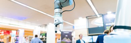 Ein moderner Roboterarm mit Greifer auf der bauma 2022, umgeben von unscharfen Besuchern und Ständen.