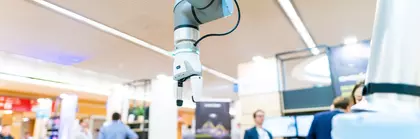 A modern robot arm with gripper at bauma 2022, surrounded by blurred visitors and stands.