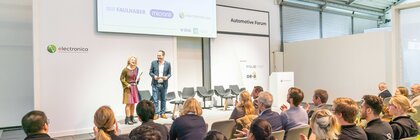 The audience in front of the stage at the electronica Automotive Forum applauds while a man and a woman stand on a presentation stage.