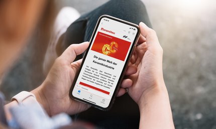 Person holding a smartphone on which a website about the ceramics industry is displayed in German.