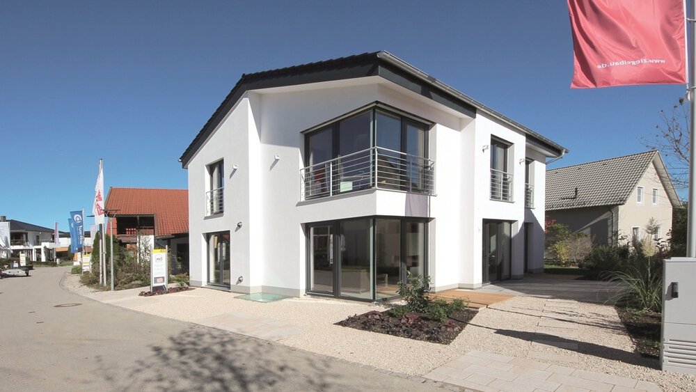 Außenansicht eines weißen zweistöckigen Wohnhauses mit großen Fensterfronten umgeben von weiteren Musterhäusern.