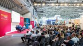 In einer Halle der transport logistic sitzt ein riesiges Publikum vor einer Bühne, auf der sechs Männer eine Diskussion abhalten.