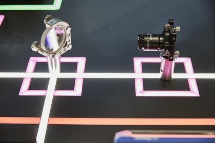 Showpiece with a laser emitter and a small glass pane at a 45° angle, mounted on a dark background with glowing lines.