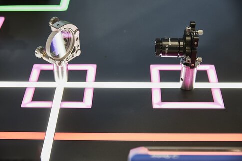Showpiece with a laser emitter and a small glass pane at a 45° angle, mounted on a dark background with glowing lines.