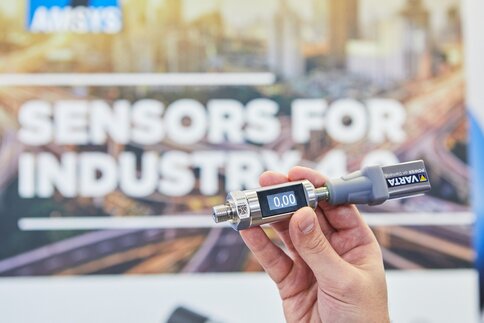 Hand holding a digital sensor in front of a blurred sign that reads 