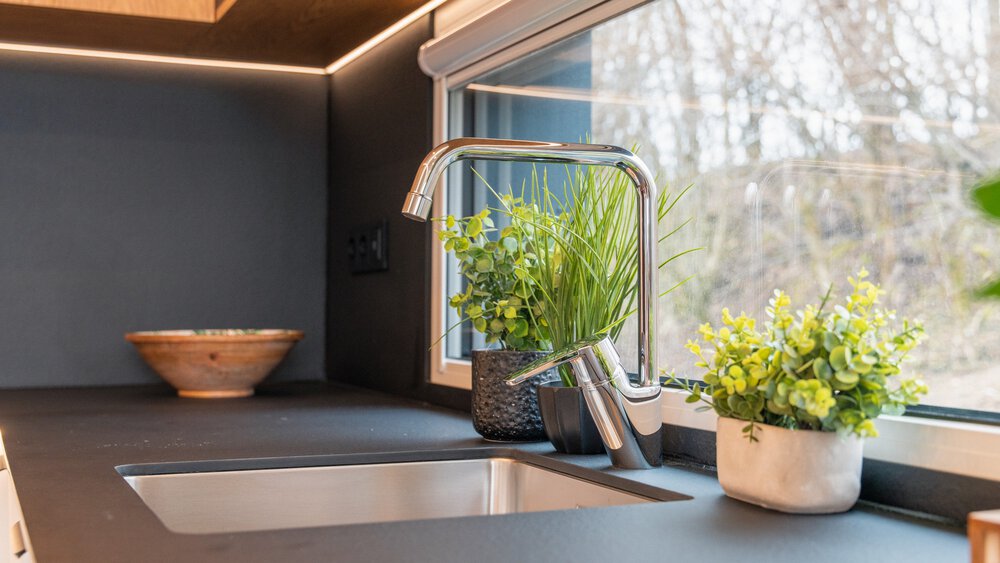Nahansicht einer schwarzen Küchenoberfläche mit einem eingelassenen Waschbecken mit silbernem Wasserhahn und einem Fenster dahinter.