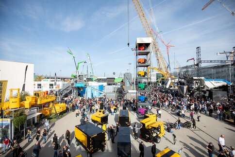 Lots of cranes and machines at a busy trade fair with numerous visitors.