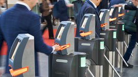 Zahlreiche Besucher stehen an einer Reihe Drehkreuzen und halten ihre Tickets unter die Ticketscanner, um das Messegelände zu betreten.