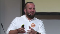 Ein bärtiger Mann mit Headset-Mikrofon spricht in einer Präsentation vertieft.