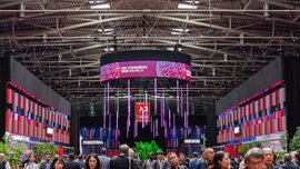 Menschen gehen durch eine belebte Kongresshalle, in der bunte Banner mit der Aufschrift „ESC-Kongress 2026 München“ hängen und über ihnen violette Lichter leuchten.