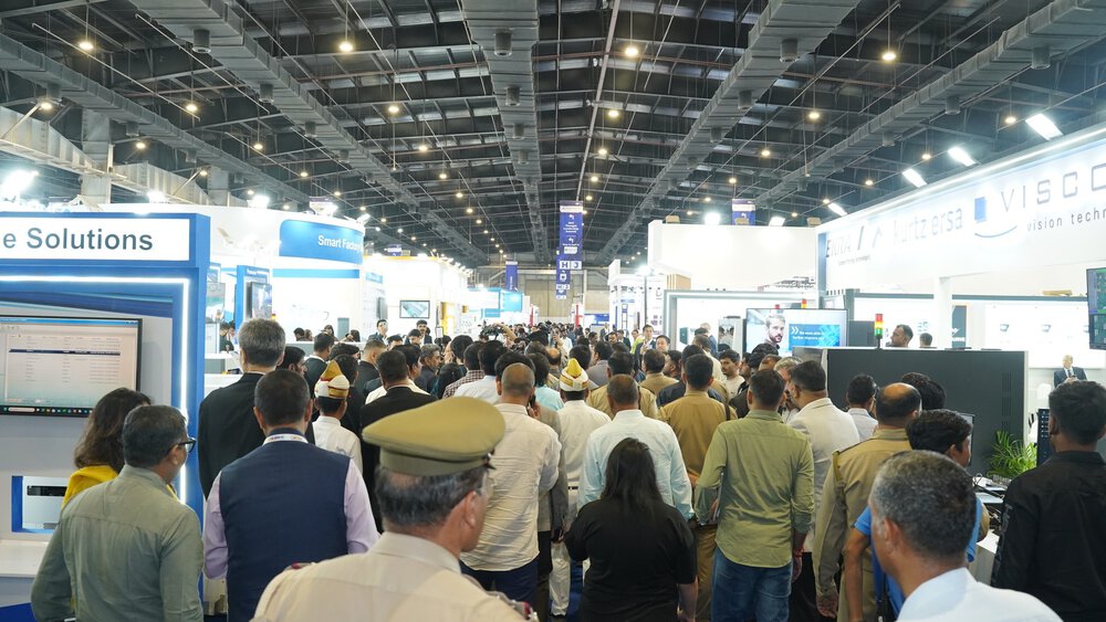 A crowd is walking through a large, covered exhibition hall with booths and bright lighting.