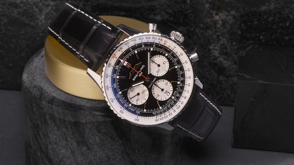 A Breitling watch with a black leather strap and detailed dial rests on a cylindrical stone stand.