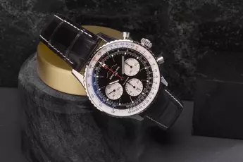 Eine Breitling-Uhr mit schwarzem Lederarmband und detailliertem Zifferblatt ruht auf einem zylindrischen Steinständer.