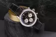 A Breitling watch with a black leather strap and detailed dial rests on a cylindrical stone stand.