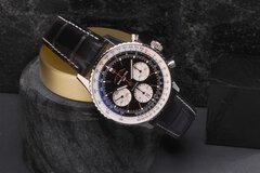 Eine Breitling-Uhr mit schwarzem Lederarmband und detailliertem Zifferblatt ruht auf einem zylindrischen Steinständer.