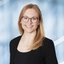 Eine lächelnde Frau mit langen blonden Haaren und runder Brille trägt ein dunkles Oberteil mit Blazer.