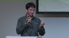 Ein Mann im dunklen Hemd steht am Rednerpult und gestikuliert mit einem Mikrofon in der Hand.