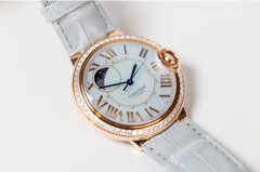 Close-up view of a delicate wristwatch with white straps, a gold-plated bezel set with gemstones, and a dial featuring the lunar cycle.