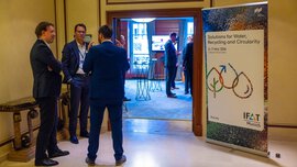 Eingangsbereich eines Veranstaltungsraums mit Gesprächen; rechts steht ein IFAT Munich-Banner, im Hintergrund ist der Raum mit Stehtischen zu sehen. 