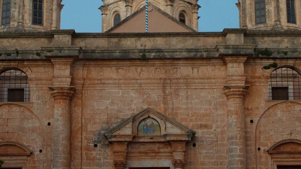 Mehrere Personen gehen bei Sonnenuntergang vor einer gewölbten Steinkirche, die von einem bogenförmigen Eingang eingerahmt wird.