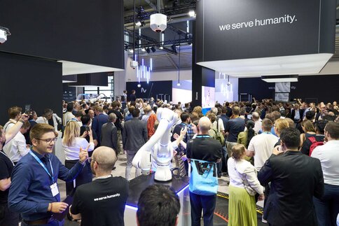 A large crowd gathers at the NEURA Robotics booth at automatica around a robotic arm on display.
