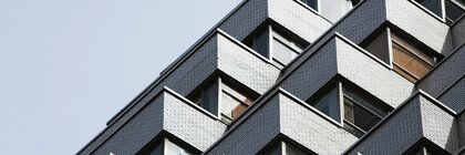 Modernes Gebäude mit geometrischen, gestaffelten Fenstern und weißer Backsteinfassade vor einem klaren Himmel.