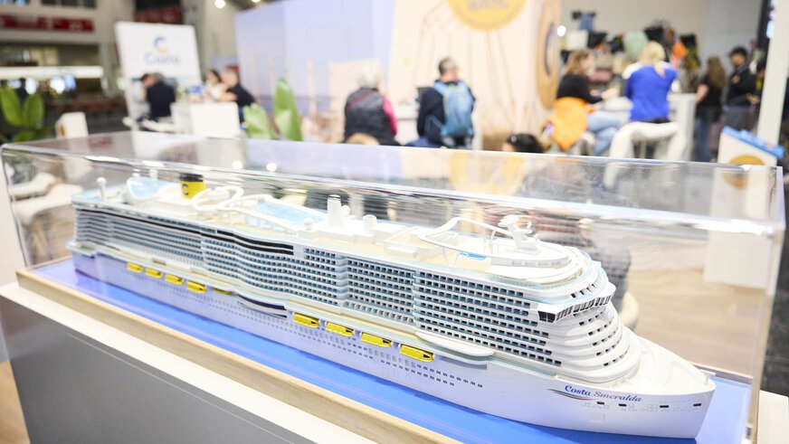 Model of a cruise ship in a glass case at a trade fair stand, with the name Costa Smeralda.