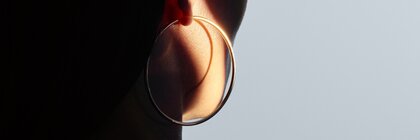 A close-up of a woman's ear wearing a large round earring, illuminated by soft light.