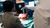 Demonstration of a medical surgical application at an exhibition booth with monitors and an anatomical model