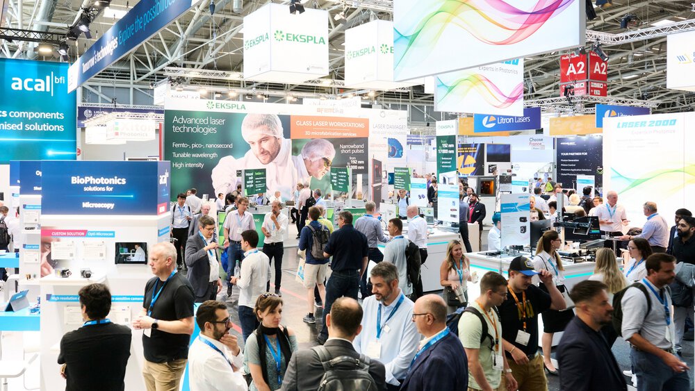 Eine Menschenmenge, die sich auf einer belebten Technologiemesse mit Ständen und Bannern verschiedener Unternehmen unterhält.