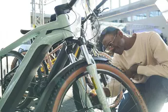 Links ist die Hälfte eines Fahrrades zu sehen, rechts ein Mann, der sich das Vorderrad des Fahrrads genauer anschaut.