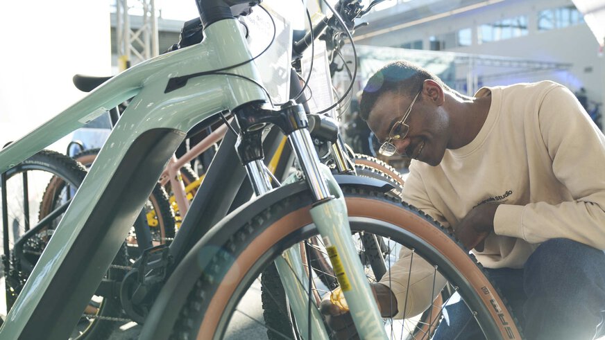 On the left is half of a bicycle, on the right a man taking a closer look at the front wheel of the bicycle.