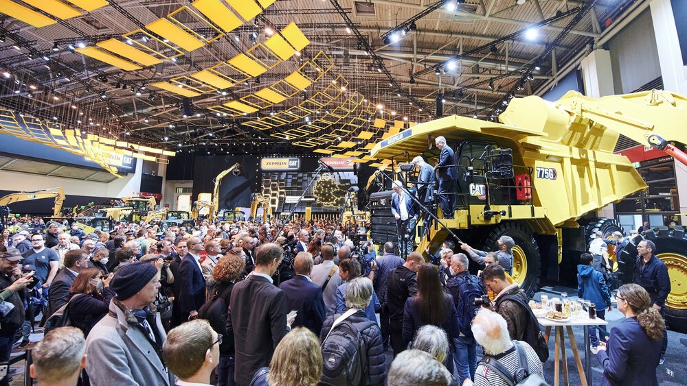 Eine große Ansammlung Presseleute drängt sich um eine große gelbe Baumaschine auf der bauma. Drei Männer steigen von der Baumaschine herab.