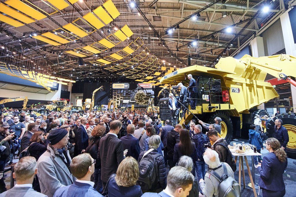 Eine große Ansammlung Presseleute drängt sich um eine große gelbe Baumaschine auf der bauma. Drei Männer steigen von der Baumaschine herab.