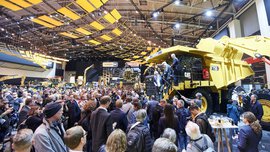 Eine große Ansammlung Presseleute drängt sich um eine große gelbe Baumaschine auf der bauma. Drei Männer steigen von der Baumaschine herab.