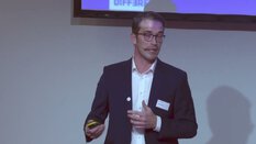 Ein Mann im Anzug spricht in einem Headset-Mikrofon und hält während einer Präsentation einen Clicker.