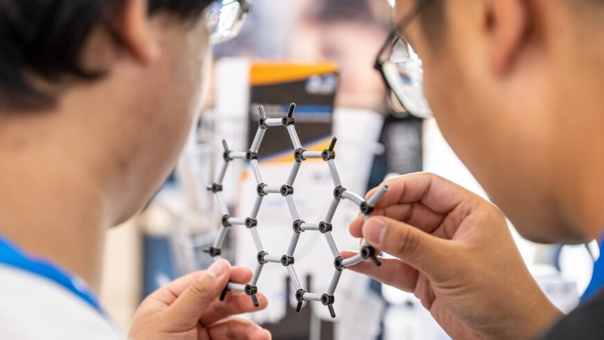 Two men hold a hexagonal grid of plastic connectors.