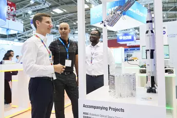 Three men at an exhibition stand look at a space shuttle model and discuss accompanying projects.