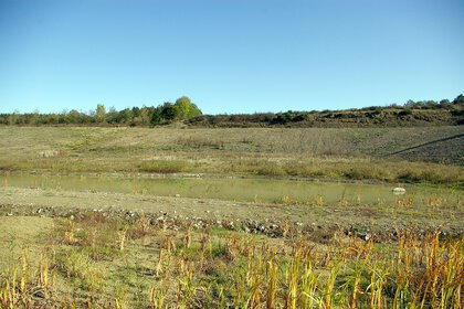A small pond on dry, barren terrain with little vegetation and a clear blue sky.